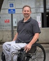 Photo of Eric Lantz in front of a handicap parking sign while sitting in his wheelchair