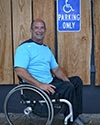 Photo of Michael Haynes in front of a handicap parking sign while sitting in his wheelchair