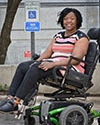 Photo of Regina Blye in front of a handicap parking sign while sitting in her motorized wheelchair